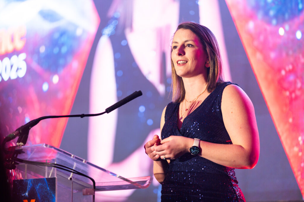 Woman in navy sleeveless dress speaking at a podium with colourful blurred background