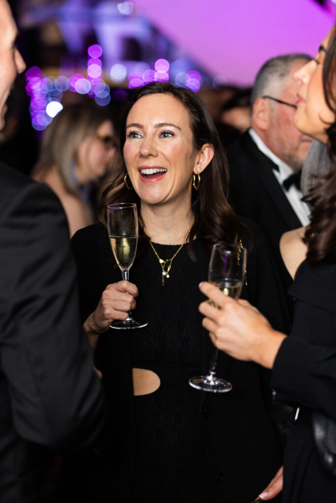 Woman holding a glass of champagne, smiling and conversing at a formal event with purple lighting