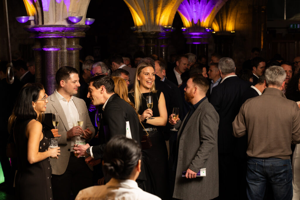 Group of people socialising with drinks under stone arches lit by purple lights