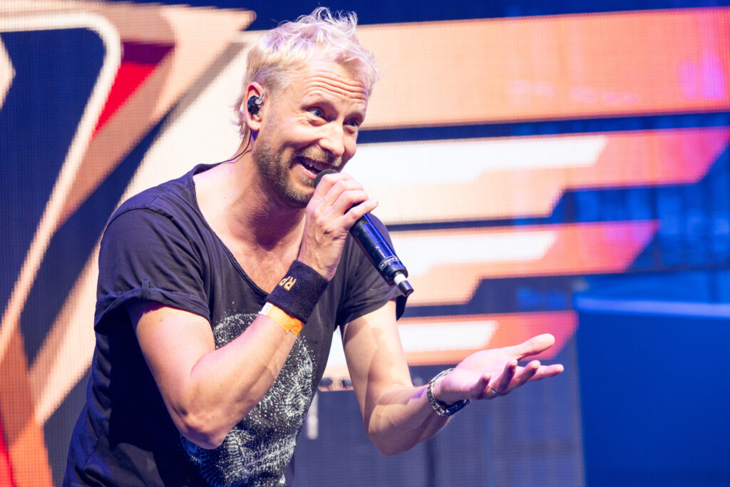 Man with microphone speaking and gesturing on stage at an event