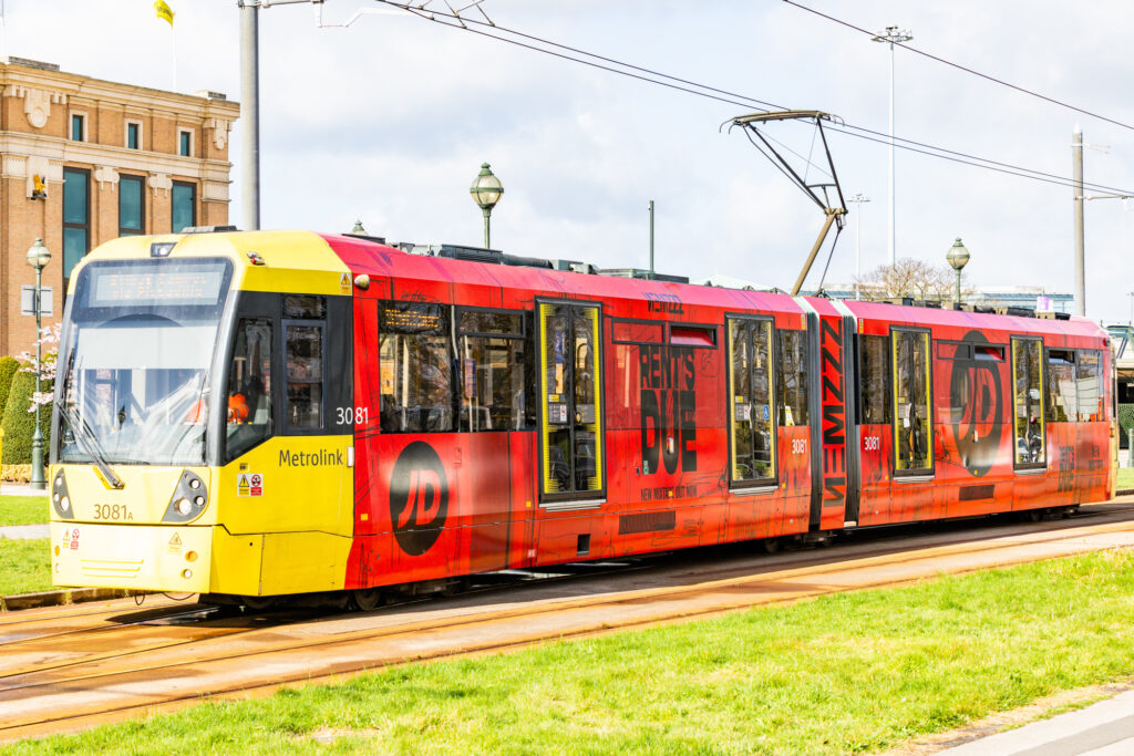 Red and yellow Metrolink tram with JD Sports advertisement on city street tracks