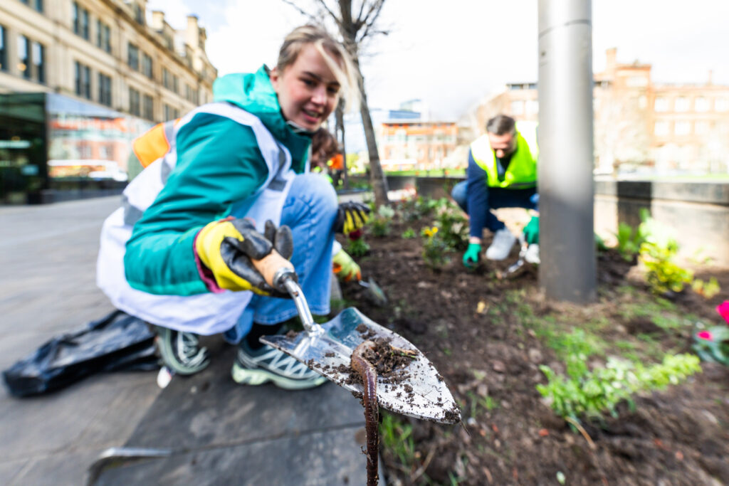 Person holding a gardening trowel with an earthworm in an urban flowerbed