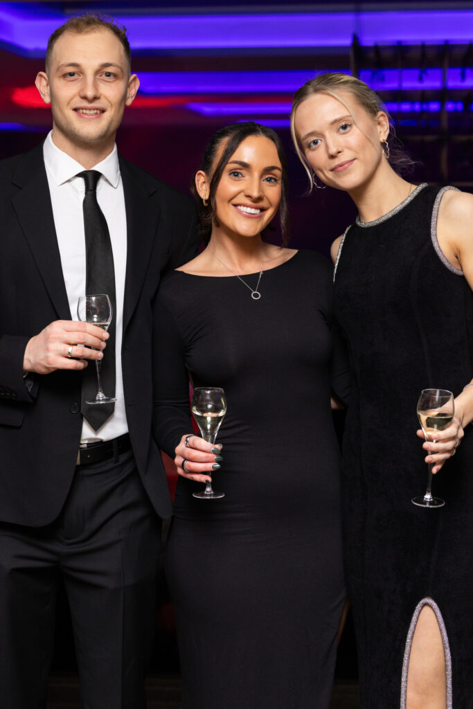 Three people dressed formally holding glasses of champagne at an indoor event
