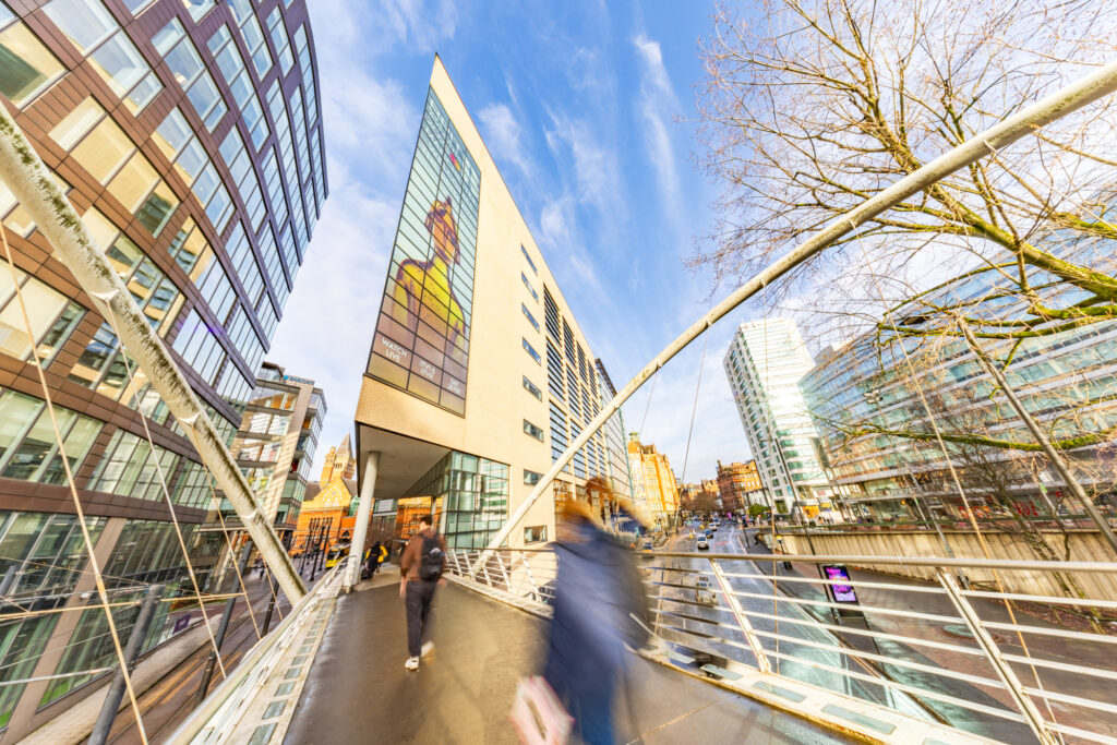 People walking on modern pedestrian bridge beside tall office buildings under blue sky