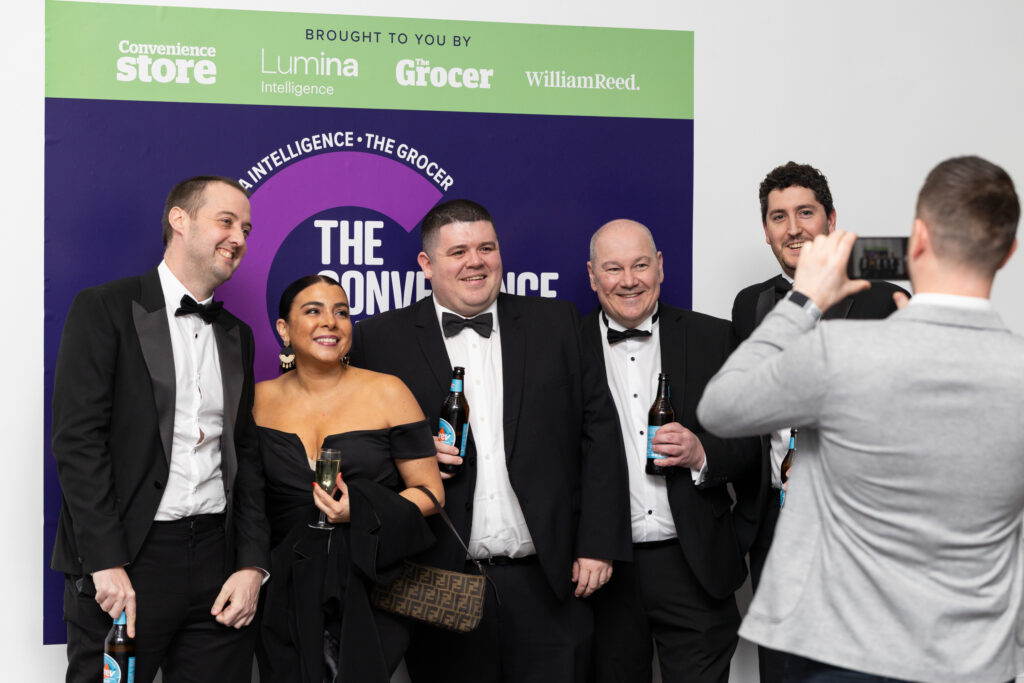 Group of people in formalwear posing for photo at an event with branded backdrop