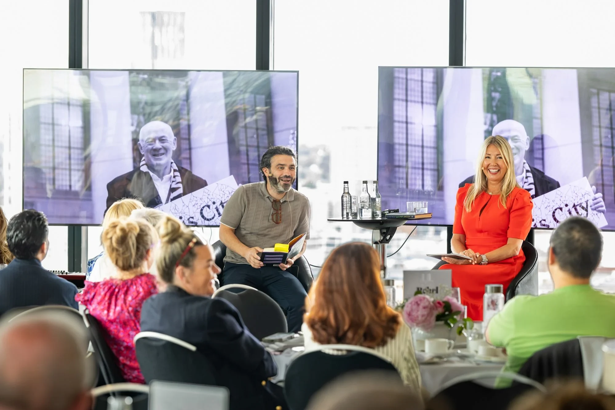 Two hosts engage an attentive audience during the We Built This City afternoon tea and Q&A at Cloud 23, The Manchester Deansgate Hotel.